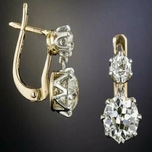 Peut inclure: Une paire de boucles d'oreilles pendantes en or avec deux pierres rondes à facettes transparentes chacune. La pierre supérieure est plus petite et sertie dans un panier en or, tandis que la pierre inférieure plus grande est suspendue.