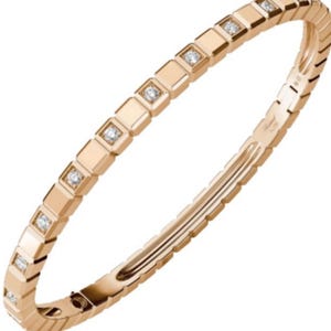 Może przedstawiać: Bransoletka typu bangle z różowego złota z powtarzającym się geometrycznym wzorem kwadratów wzdłuż zewnętrznej obręczy. Niektóre kwadratowe segmenty są ozdobione małymi, okrągłymi, przezroczystymi diamentami. Metal ma polerowane wykończenie i zapięcie na zawiasie.