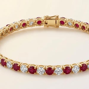 Pode incluir: Uma pulseira de ténis em ouro com um padrão alternado de rubis vermelhos redondos e diamantes brancos transparentes cravados numa linha contínua. A pulseira inclui um mecanismo de fecho de caixa seguro com trinco de segurança em ouro.