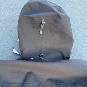 May include: Close-up of a black hooded jacket. The hood is up, revealing a drawstring and a small, decorative toggle. The jacket appears to be made of a durable, water-resistant material. The hood is attached to the jacket with a seam.
