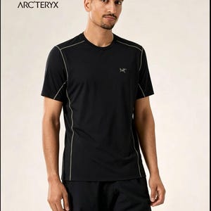 May include: Black athletic t-shirt with grey trim and the Arc'teryx logo. The shirt has a crew neck and short sleeves. The model is wearing black athletic trousers. The Arc'teryx logo is visible on the upper left and lower right of the shirt.