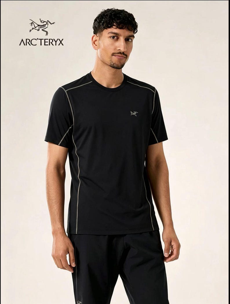 May include: Black athletic t-shirt with grey trim and the Arc'teryx logo. The shirt has a crew neck and short sleeves. The model is wearing black athletic trousers. The Arc'teryx logo is visible on the upper left and lower right of the shirt.