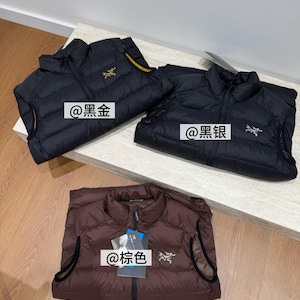 May include: Three lightweight puffer vests in black and brown are displayed. The black vests have gold and silver logos, and the brown vest has a silver logo. Each vest has a zipper closure and a high collar. The text "@黑金", "@黑银", and "@棕色" are visible.
