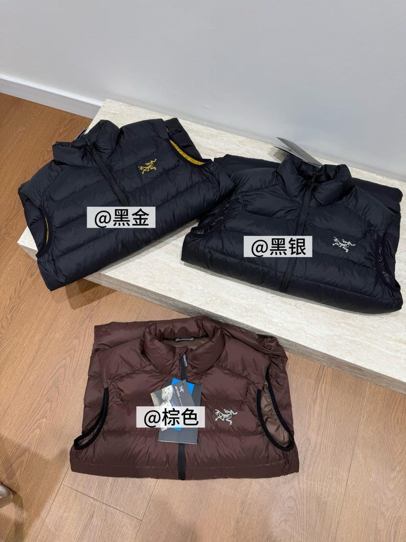 May include: Three lightweight puffer vests in black and brown are displayed. The black vests have gold and silver logos, and the brown vest has a silver logo. Each vest has a zipper closure and a high collar. The text "@黑金", "@黑银", and "@棕色" are visible.