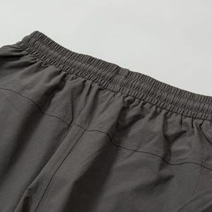 Pode incluir: Close-up da cintura e da parte superior de cal&ccedil;as esportivas cinza escuro. A cintura el&aacute;stica &eacute; franzida e costurada, com um canal para o cord&atilde;o. O tecido parece leve e ligeiramente texturizado, com costuras verticais.