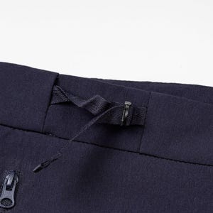Pu&ograve; includere: Primo piano di pantaloni sportivi blu navy. La cintura presenta un cordino e una chiusura in metallo. Una tasca con cerniera &egrave; visibile sul lato sinistro. Il tessuto ha una trama sottile.