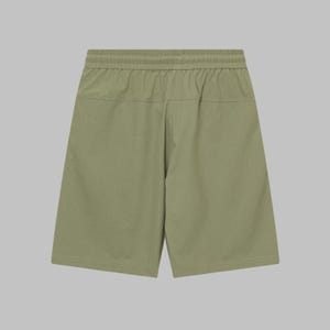 Pode incluir: Cal&ccedil;&otilde;es verde-oliva com c&oacute;s el&aacute;stico. Os cal&ccedil;&otilde;es t&ecirc;m um ajuste descontra&iacute;do e um design simples. O tecido parece ser um material leve, adequado para climas quentes. Os cal&ccedil;&otilde;es s&atilde;o exibidos em um fundo neutro.