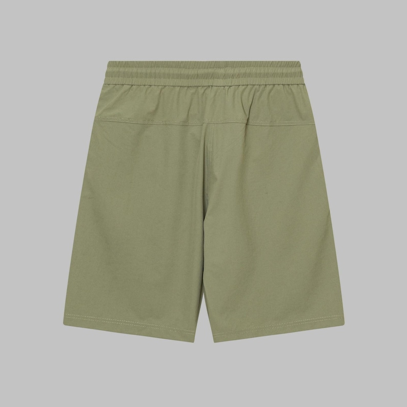 Pode incluir: Cal&ccedil;&otilde;es verde-oliva com c&oacute;s el&aacute;stico. Os cal&ccedil;&otilde;es t&ecirc;m um ajuste descontra&iacute;do e um design simples. O tecido parece ser um material leve, adequado para climas quentes. Os cal&ccedil;&otilde;es s&atilde;o exibidos em um fundo neutro.