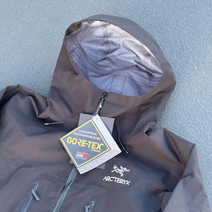 May include: Black hooded jacket with a zipper closure and two front pockets. The jacket features the GORE-TEX logo and the Arc'teryx logo. The jacket is made of a durable, waterproof material.