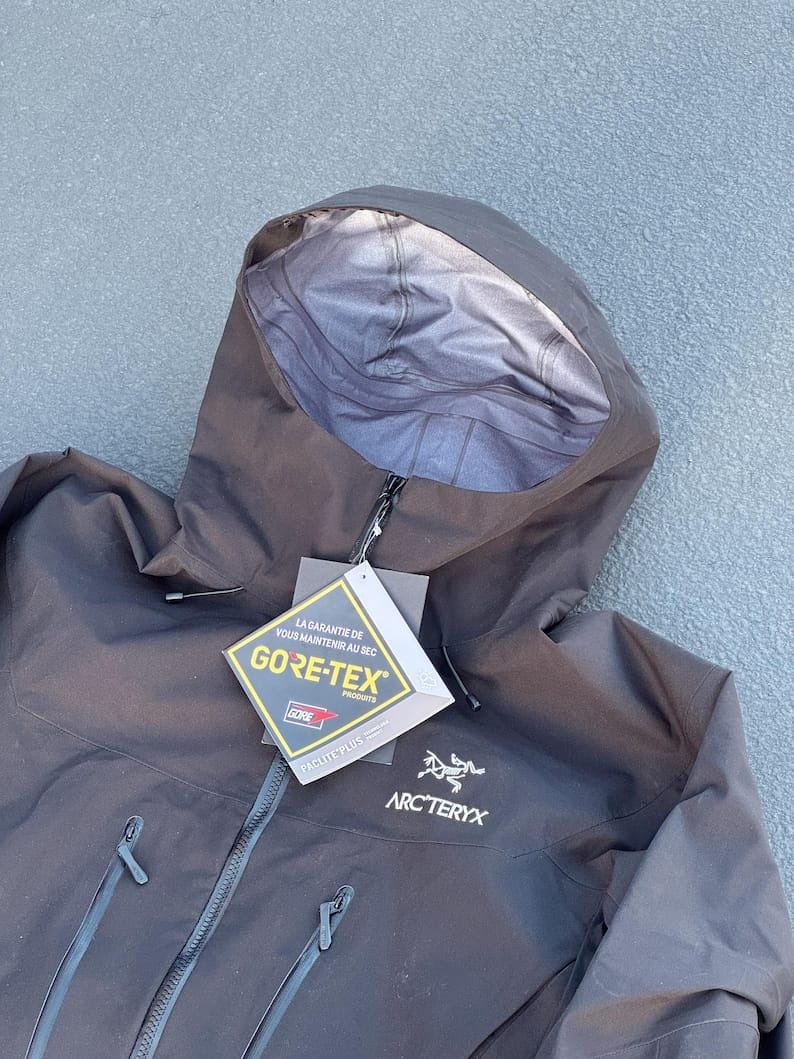 May include: Black hooded jacket with a zipper closure and two front pockets. The jacket features the GORE-TEX logo and the Arc'teryx logo. The jacket is made of a durable, waterproof material.
