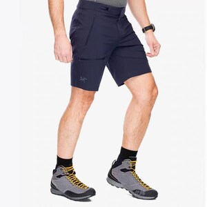 Pu&ograve; includere: Pantaloncini blu navy con tasche con cerniera e un piccolo logo. I pantaloncini sono abbinati a scarponi da trekking grigi con lacci gialli e calzini neri. Un orologio nero &egrave; visibile al polso.