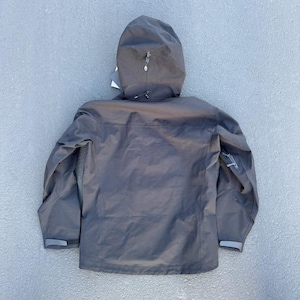 May include: A dark gray hooded jacket with a zipper closure and a small logo on the sleeve. The jacket has a hood with a drawstring and adjustable cuffs. The jacket is made of a lightweight, waterproof material.