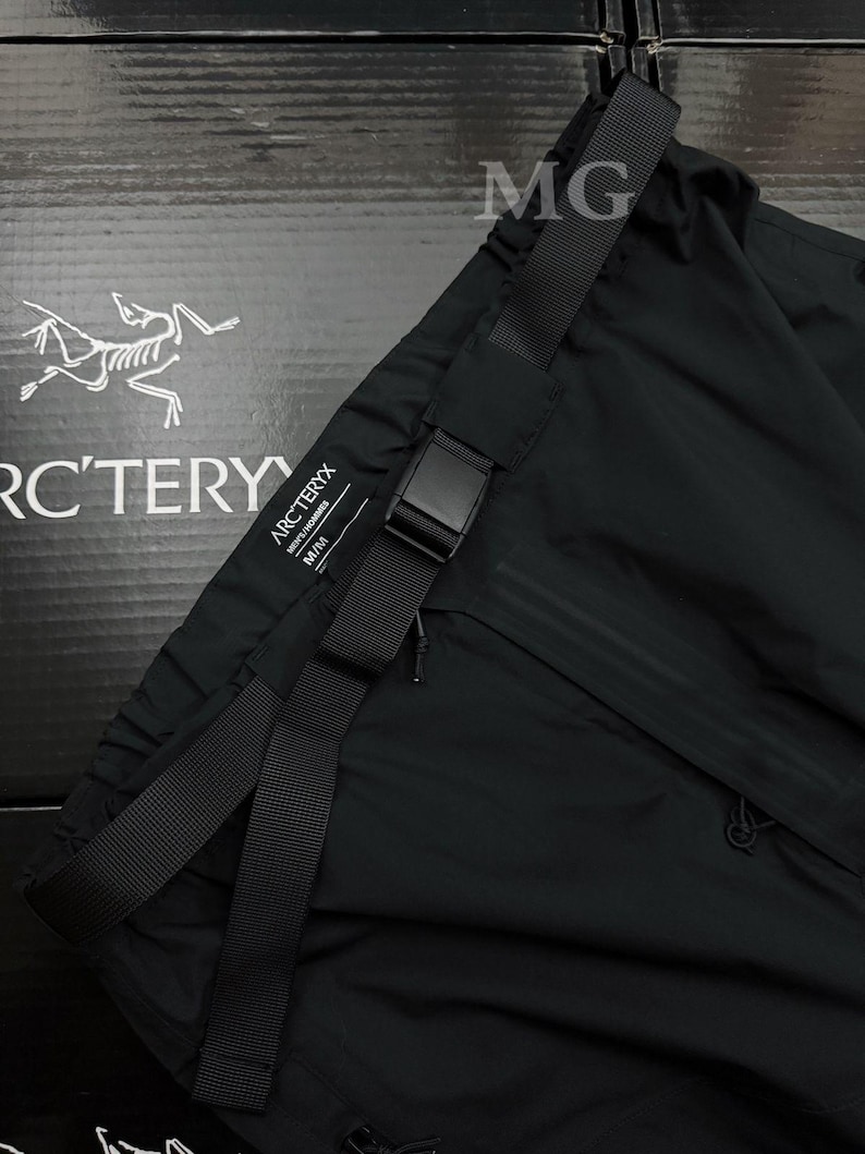 May include: Black athletic pants with a black adjustable belt and buckle. The pants have a small zipper pocket and the brand name "Arc'teryx" is visible. The pants are made of a lightweight material.