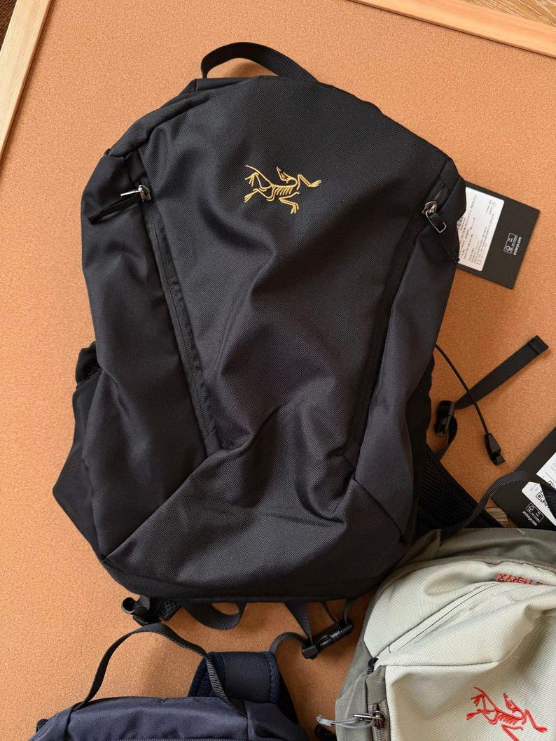 May include: Black backpack with a gold logo on the front. The backpack has a top handle, two zippered compartments, and adjustable straps. The backpack is made of a durable material and is suitable for everyday use.