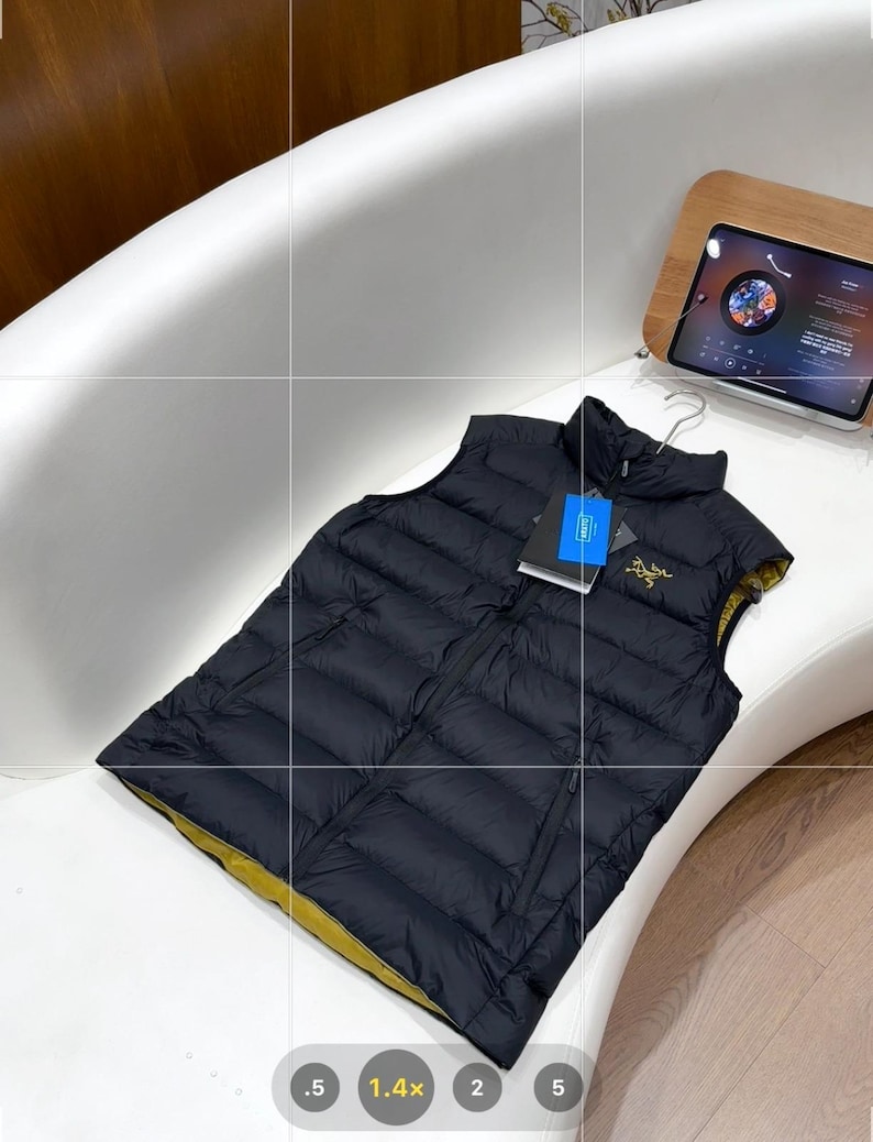 May include: A black puffer vest with a yellow lining, displayed on a white surface. The vest has a zip closure and a small logo on the chest. A tag is attached. The vest is likely designed for outdoor activities.