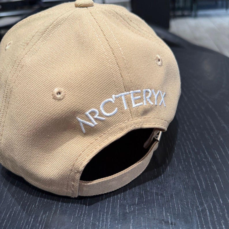 Puede incluir: Gorra de b&eacute;isbol beige con la palabra "ARCTERYX" bordada en blanco en la parte trasera. La gorra tiene una visera curva y una correa ajustable. Fabricada con un tejido resistente.