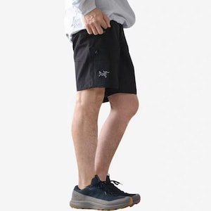 Pu&ograve; includere: Pantaloncini sportivi neri con un piccolo logo sulla gamba sinistra. I pantaloncini hanno tasche e sono indossati con scarpe sportive blu scuro. La persona indossa una camicia a maniche lunghe azzurra.