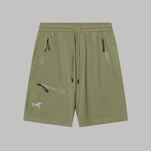 Pode incluir: Cal&ccedil;&otilde;es verde-oliva com cintura com cord&atilde;o e v&aacute;rios bolsos com z&iacute;per. Os cal&ccedil;&otilde;es apresentam um pequeno log&oacute;tipo branco na perna esquerda. O tecido parece leve e adequado para atividades ao ar livre.