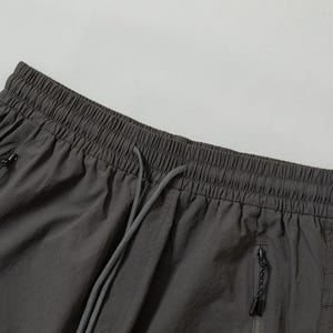 Pode incluir: Close-up de cal&ccedil;&otilde;es desportivos cinza carv&atilde;o. Os cal&ccedil;&otilde;es t&ecirc;m uma cintura el&aacute;stica com cord&atilde;o, dois bolsos com z&iacute;per e um pequeno bolso lateral. O tecido parece leve.