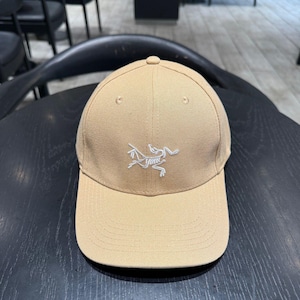 Puede incluir: Gorra de b&eacute;isbol beige con visera curva. La gorra presenta un logotipo blanco bordado en la parte delantera. La gorra est&aacute; hecha de una tela duradera y tiene un dise&ntilde;o cl&aacute;sico de seis paneles. La gorra es de color neutro.