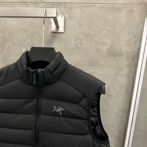 May include: Black puffer vest with a high collar and a zipper closure. The vest features a small logo on the chest. The vest is sleeveless and appears to be made of a quilted material. The vest is hanging on a black hanger.