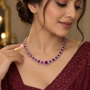Puede incluir: Un collar que presenta una serie de piedras preciosas redondas de color rosa intenso, cada una rodeada por un halo de pequeñas piedras blancas transparentes engastadas en un marco de metal plateado, dispuestas en degradado con una piedra central.