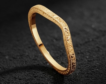 May include: A gold-colored ring with a unique, square-shaped design. The ring features an intricate, engraved floral pattern along the outer edges. The ring is displayed on a dark, textured surface.