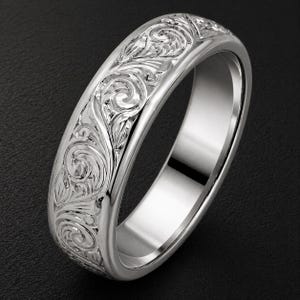 Könnte beinhalten: Ein polierter silberfarbener Ring mit einem komplizierten, durchgehenden gravierten Rankenmuster auf dem äußeren Band. Die Innenseite des Rings ist glatt und reflektierend und weist ein hochglänzendes metallisches Finish auf.