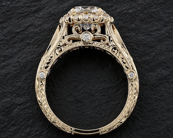 May include: A yellow gold ring featuring a large round center stone surrounded by a halo of smaller diamonds. The band and gallery are decorated with intricate filigree scrollwork and milgrain detailing, with additional small diamonds set along the sides.