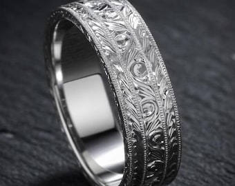 May include: A silver-toned metal ring featuring an intricate, repeating engraved leaf pattern across the outer band. The edges of the ring are defined by a fine, beaded milgrain texture that frames the central floral-inspired design.