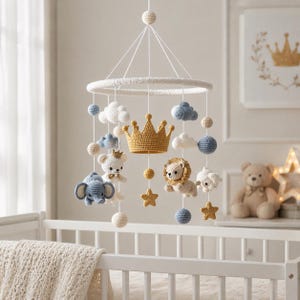 May include: A handmade baby mobile featuring crocheted elements. The mobile includes a yellow crown, clouds, stars, and animal figures like a bear, elephant, and lion. The color palette consists of white, blue, and yellow, creating a soft, nursery-themed aesthetic.