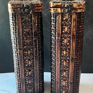 May include: Two tall, rectangular storage containers crafted from dark brown woven material with a distressed finish. Each container features a hinged lid secured by a metal latch and a small metal handle on top, showcasing a complex, textured weave.