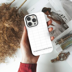 Può includere: Custodia bianca per iPhone con motivo a griglia e la scritta "=IF(MONDAY,COFFEE,WINE)". La custodia ha un modulo fotocamera nero. Lo sfondo include una rivista, un orologio e una penna.