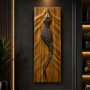 May include: A rectangular wooden wall art piece featuring a three-dimensional carved alligator in a dark, textured finish. The alligator is centred on a light brown, vertically grained wooden board with carved ripples surrounding the figure.