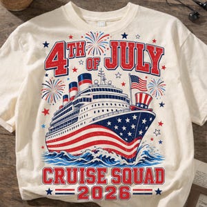 May include: A cream-colored t-shirt featuring a graphic of a cruise ship decorated with American flag patterns, surrounded by fireworks and stars. The text reads 4th OF JULY CRUISE SQUAD 2026 in red, with a small American flag and top hat.