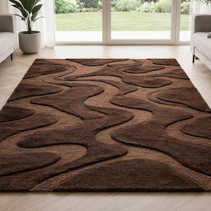 May include: A rectangular area rug featuring a deep brown and tan color palette with a raised, carved-style abstract wave pattern. The rug has a thick, textured pile that creates a multi-dimensional surface with flowing, organic shapes throughout.