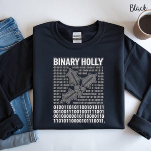 May include: A black crewneck sweatshirt featuring the white text "BINARY HOLLY" above a graphic of three holly leaves filled with binary code. Additional rows of binary code are printed below the holly graphic. The garment has a Gildan brand label.