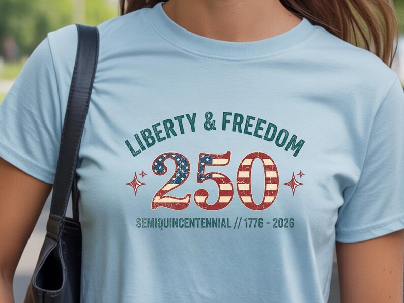 Puede incluir: Camiseta azul claro con las palabras "Liberty & Freedom" sobre el n&uacute;mero "250" en rojo, blanco y azul, con el texto "Semiquincentennial // 1776-2026" debajo. La camiseta tiene cuello redondo y mangas cortas.