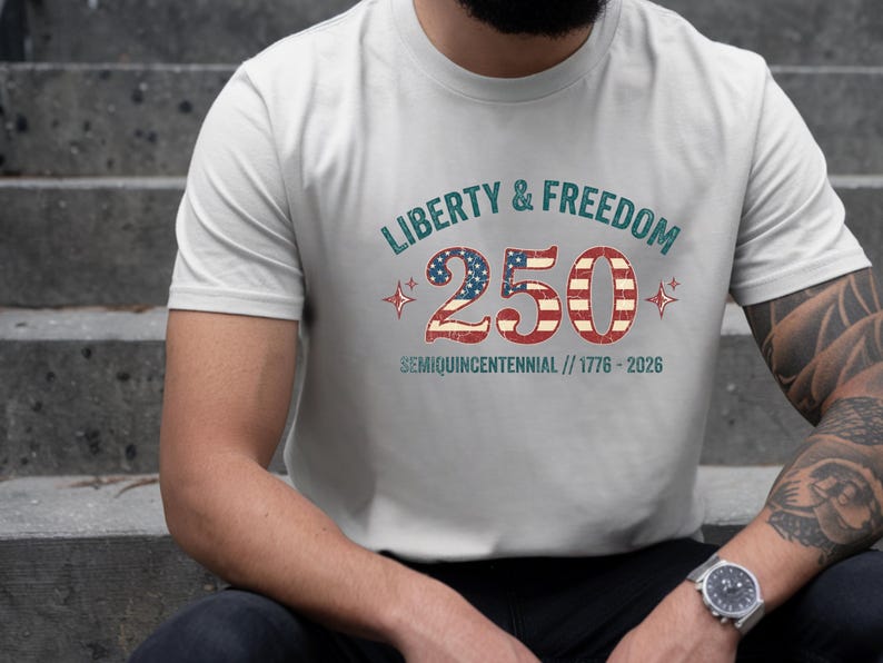 Puede incluir: Camiseta gris claro con el texto "LIBERTY & FREEDOM 250 SEMIQUICENTENNIAL // 1776-2026" en rojo, blanco y azul. El n&uacute;mero 250 est&aacute; dise&ntilde;ado con la bandera americana. La camiseta es de cuello redondo.