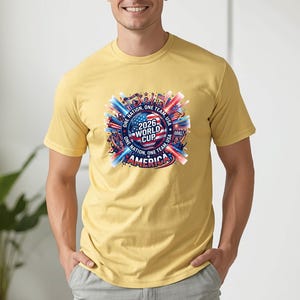 May include: Mustard yellow t-shirt featuring a colorful graphic for the 2026 World Cup in America. The design includes flags, the text "2026 World Cup America", and the phrases "One Nation, One Team, USA".