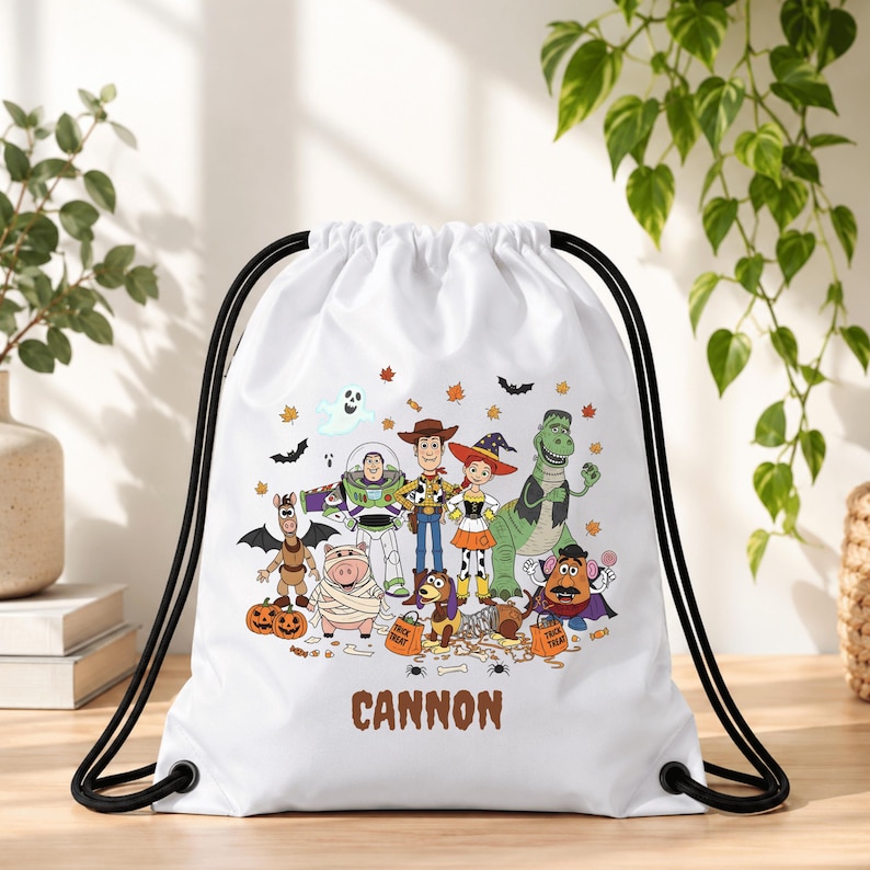 May include: A white drawstring bag featuring a colorful Halloween-themed graphic of Toy Story characters including Woody, Buzz Lightyear, Jessie, Rex, and Mr. Potato Head in costumes, with the name CANNON printed in brown letters at the bottom.