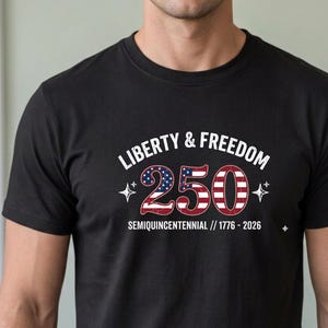 Puede incluir: Camiseta negra con el texto "LIBERTY & FREEDOM" sobre el n&uacute;mero "250" en rojo, blanco y azul, con el texto "SEMIQUINCENTENNIAL // 1776 - 2026" debajo.