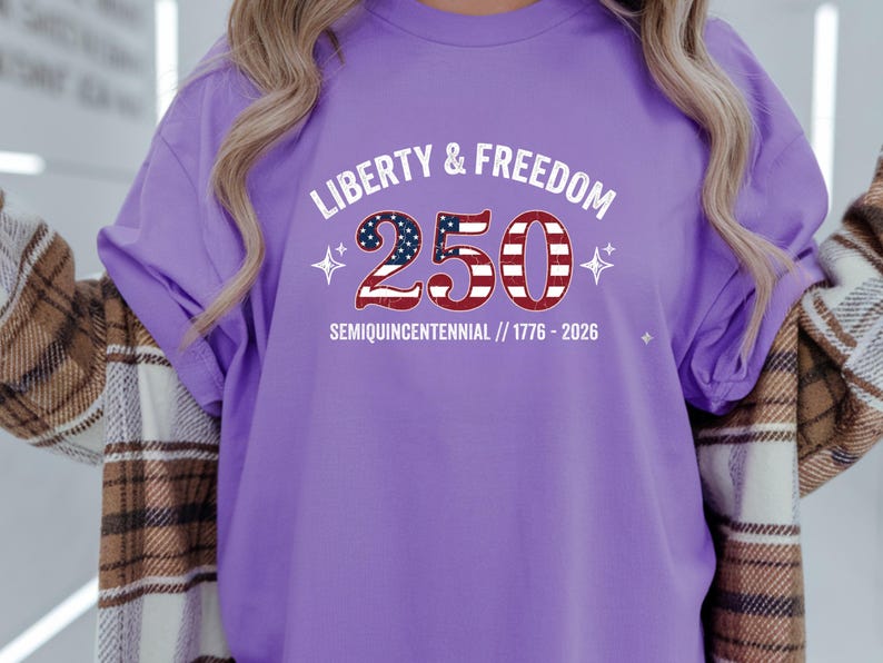 Puede incluir: Camiseta lila con la inscripci&oacute;n "LIBERTY & FREEDOM 250 SEMIQUICENTENNIAL // 1776-2026". El n&uacute;mero 250 est&aacute; dise&ntilde;ado con un patr&oacute;n de bandera americana roja, blanca y azul. La camiseta tiene mangas cortas.