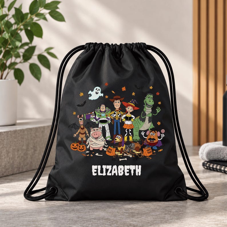 May include: A black drawstring backpack featuring a colorful graphic of various animated toy characters dressed in Halloween costumes, including pumpkins, a ghost, and bats. The name ELIZABETH is printed in white capital letters at the bottom.