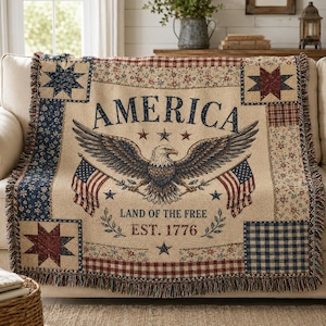 May include: A beige throw blanket with an American flag theme. The blanket features an eagle, the word "AMERICA", and the text "LAND OF THE FREE EST. 1776". It has a fringed edge and patchwork design with stars and floral patterns.