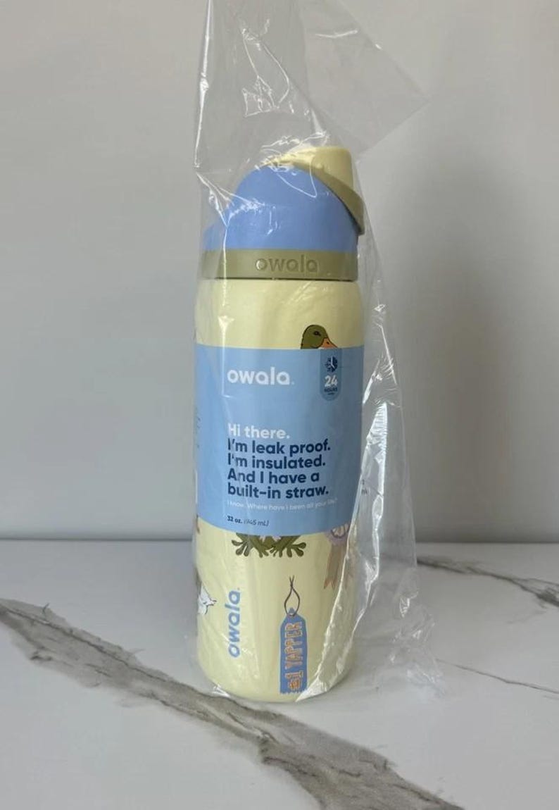 May include: A yellow and blue Owala water bottle with a built-in straw, packaged in clear plastic. The bottle has the text "Hi there. I'm leak proof. I'm insulated. And I have a built-in straw."