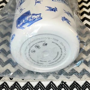 Op de afbeelding: Witte waterfles met blauwe illustraties van katten, insecten en andere ontwerpen. De fles is 946,5 ml en heeft de tekst "BPA-vrij" en "Made in China". De fles zit in een doorzichtige plastic zak.