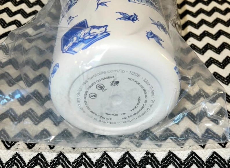 Op de afbeelding: Witte waterfles met blauwe illustraties van katten, insecten en andere ontwerpen. De fles is 946,5 ml en heeft de tekst "BPA-vrij" en "Made in China". De fles zit in een doorzichtige plastic zak.