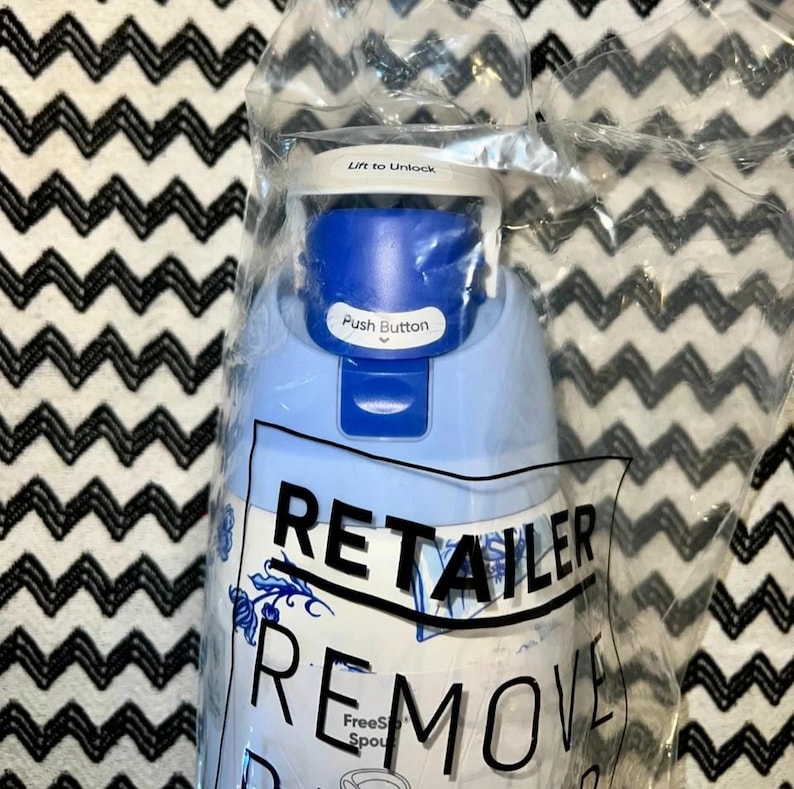 Op de afbeelding: Een blauw-witte waterfles met een drukknop en de tekst "Lift to Unlock". De fles zit in een doorzichtige plastic zak met de tekst "RETAILER REMOVE".