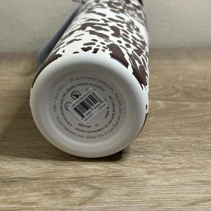 May include: A white and brown patterned water bottle. The bottle has a brown lid and a white body with brown spots. The bottom of the bottle has a label with text. The bottle is 24oz/710ml and BPA free.